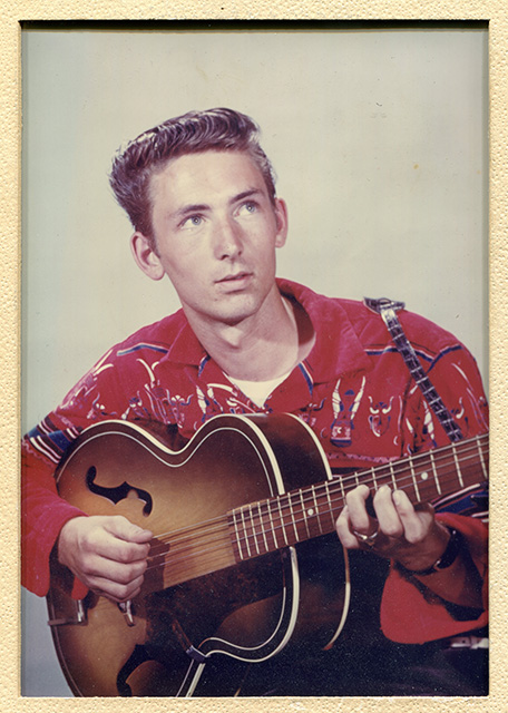 Vintage portrait of young man in red western shirt playing acoustic guitar, looking up