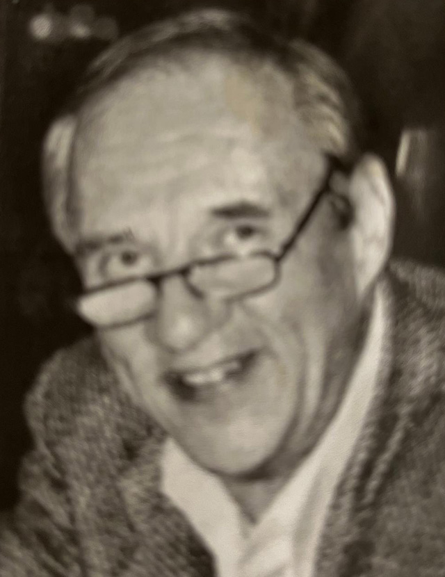 Grainy black-and-white image of an older man wearing glasses and smiling