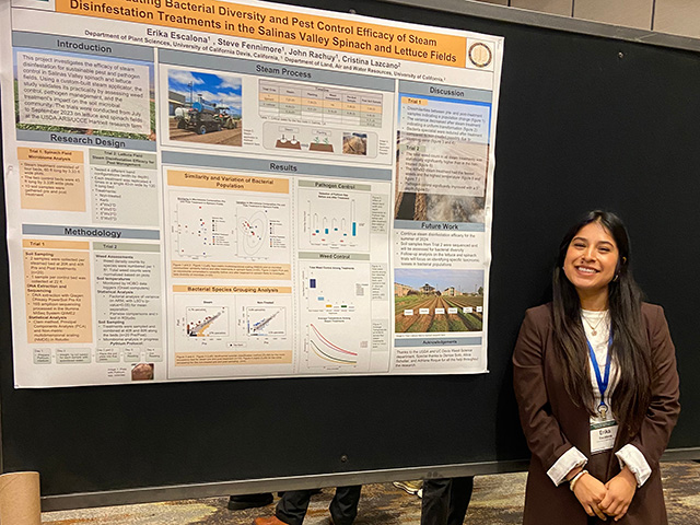 Young woman standing by a scientific poster about the impact of steam treatment on soil bacteria.