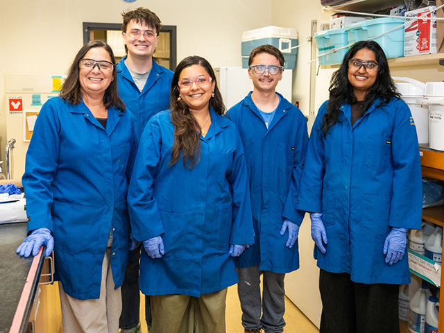 Five researchers in blue lab coats and gloves smiling, in a laboratory. UC Davis Department of Plant Sciences
