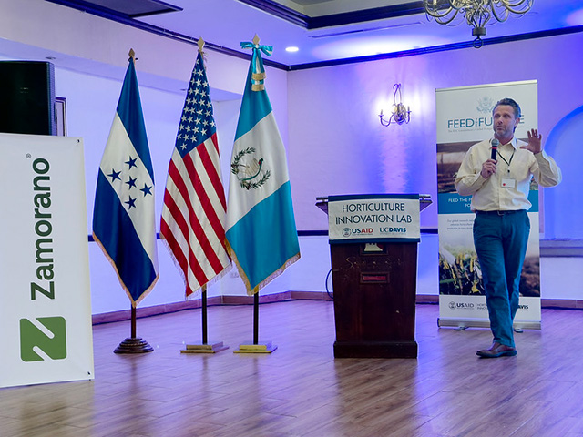 Man talking. Formal indoor setting with flags of Guatemala and the United States.
