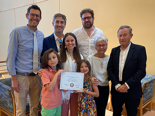 A group of people. We see children, parents, grandparents, two men and a young woman holding a paper certificate.