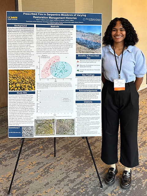 Person with curly hair stands beside a research poster in an indoor setting. UC Davis Department of Plant Sciences