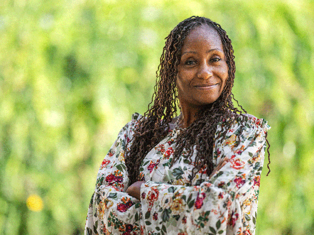 An African-American woman stands with her arms crossed in front of tall grass