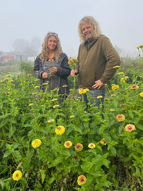 Two smiling people stand in a field of yellow flowers, surrounded by fog. UC Davis Department of Plant Sciences
