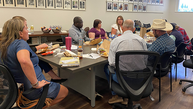 Men and women dressed casually sit around a long table in a room.