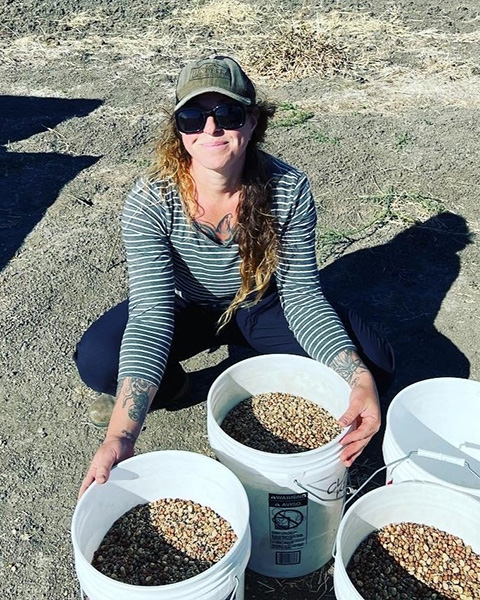 Woman squatting on the ground, with large buckets of pinto beans