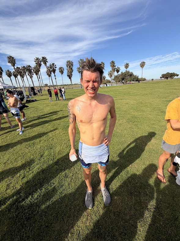 Smiling, shirtless, slender young man in blue shorts on sunny lawn with palm trees. Blue sky streaked with wispy clouds. UC Davis Department of Plant Sciences