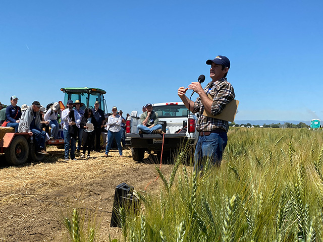 A man by a field, talking to a group of people.