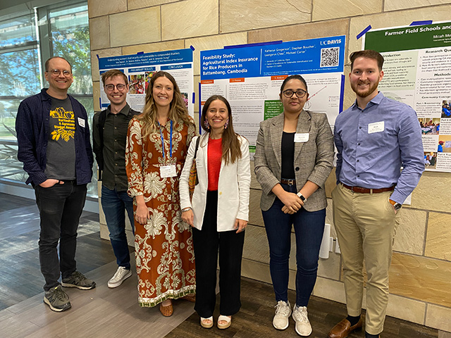 Five young men and women standing in a row in front of research posters.