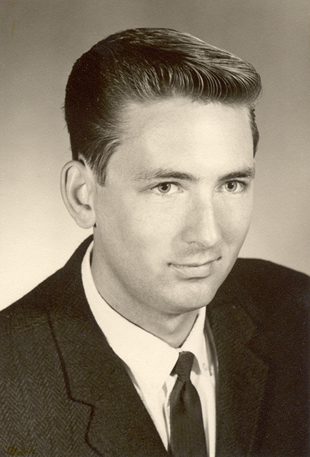 Black-and-white portrait photograph of a young man in a suit with 1960s-style haircut.