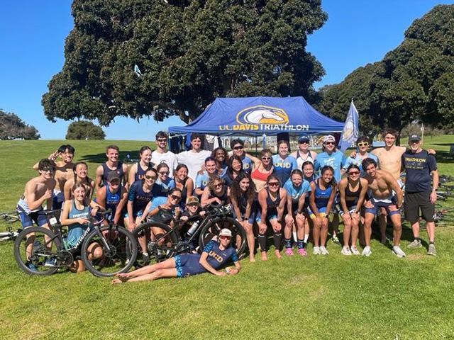 Diverse group of mostly young people at sunny park by a blue tent, athletes and bikes. UC Davis Department of Plant Sciences