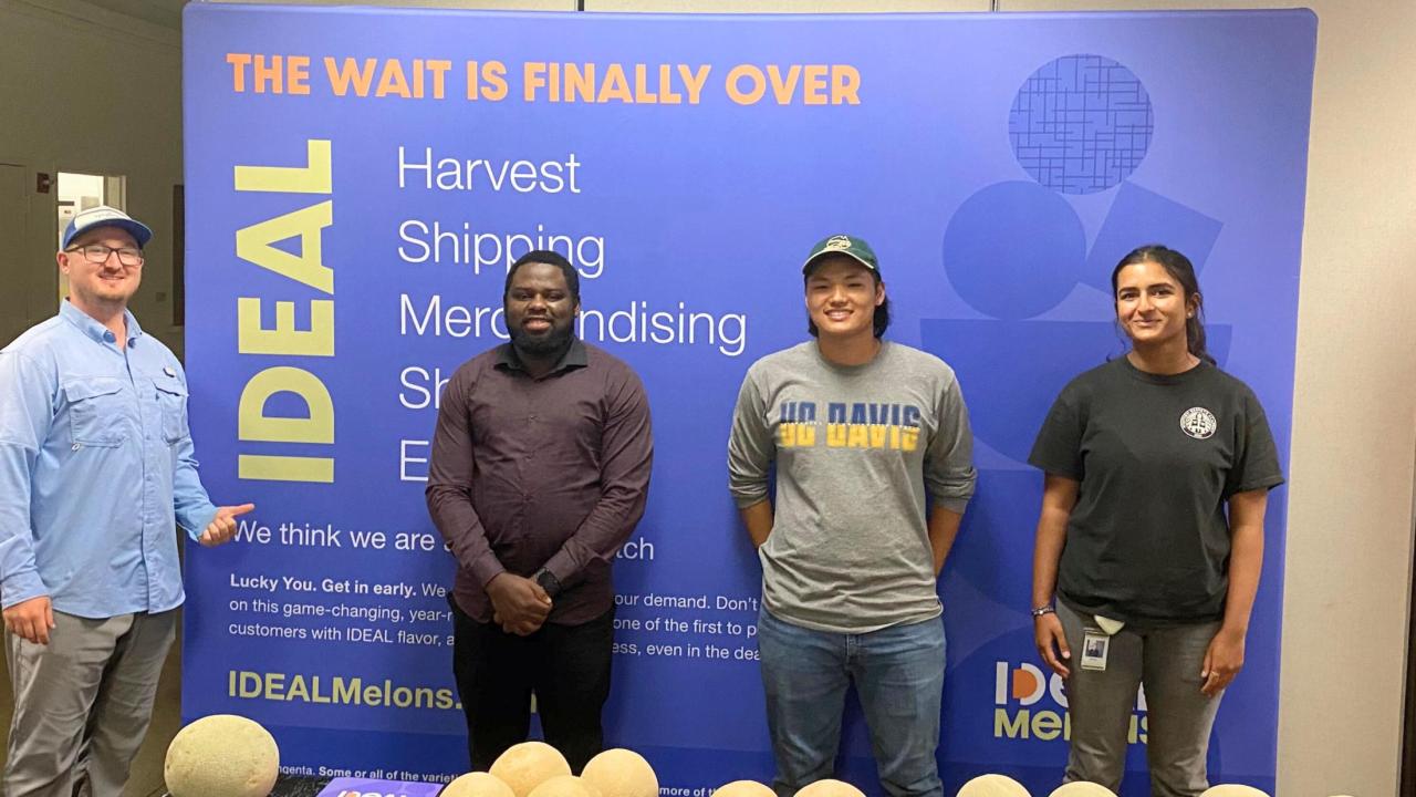 Khushi Chawda stands on the right. She is in front of a banner for her Syngenta Seeds internship. There are three other people in the photo. 