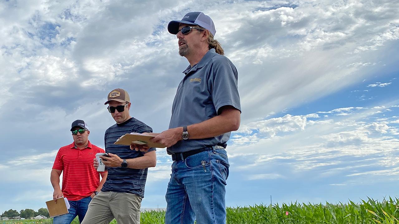 Man standing in a field against a background of dramatic clouds. Two more men look on. UC Davis Department of Plant Sciences