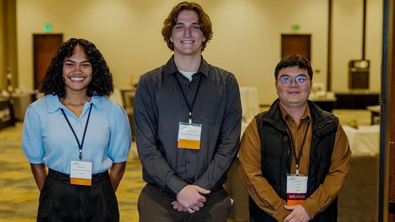 Three young adults stand together, smiling, in a conference setting. UC Davis Department of Plant Sciences