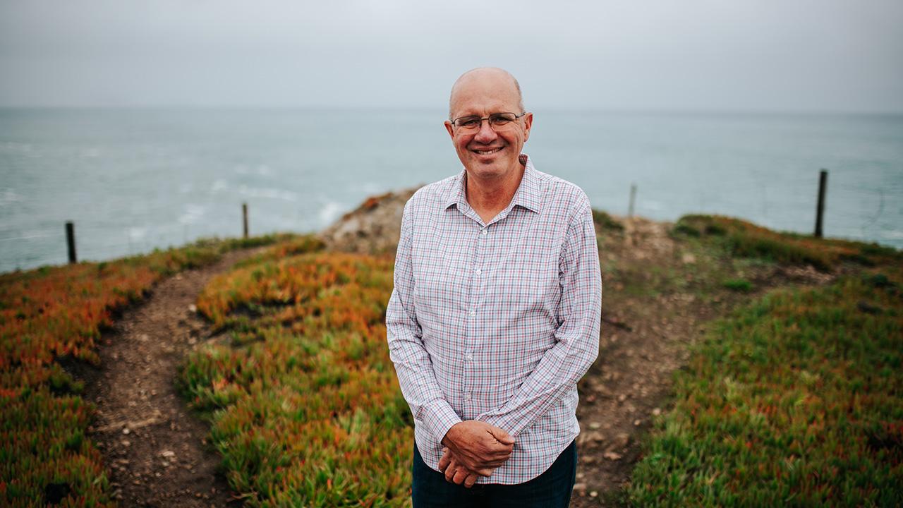 Man standing on a cliff, behind him is a gray-blue ocean 