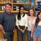 Five smiling people standing in a bright laboratory with shelves and equipment. At the back left, you can see little toy superhero figures. UC Davis Department of Plant Sciences