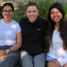 Four young women sit in a row, smiling 