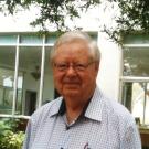 An older man in an outdoor setting smiles at the camera